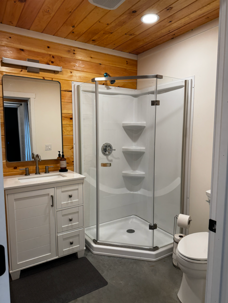 Private Groom's Den bathroom with modern vanity, glass-enclosed corner walk-in shower, and pine shiplap walls