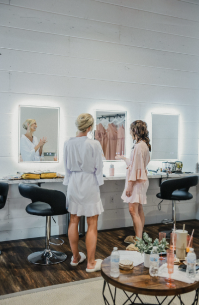 Bride and bridesmaids getting ready in front of illuminated vanity mirrors in the bridal suite