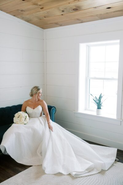 Bride seated elegantly on the bridal suite sofa holding white floral bouquet