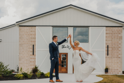 Bride and groom twirling in front of The Willow venue with stone facade and white barn doors