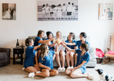 Bride and bridal party in matching royal blue loungewear toasting mimosas together on the bridal suite sofa