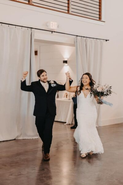 Newlyweds joyfully celebrating their grand reception entrance into the ballroom with raised hands
