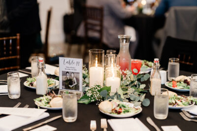 Winter wedding reception guest table setting with glowing pillar candles in hurricane glass and eucalyptus garland