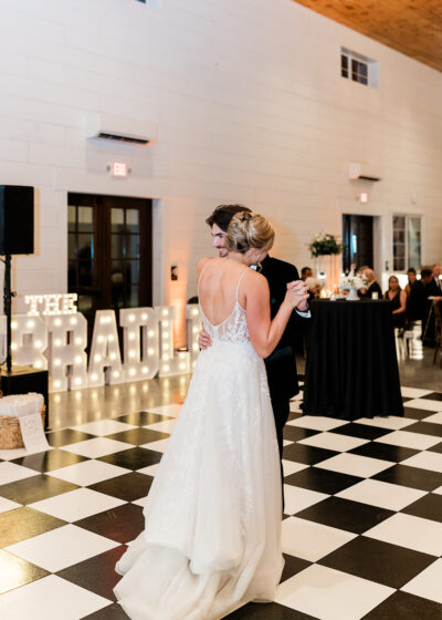 Bride and groom first dance on the black-and-white checkered dance floor with illuminated marquee letters