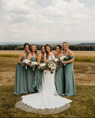 Bride with long veil and bridesmaids in sage green gowns in rolling countryside meadow overlooking Pennsylvania ridges