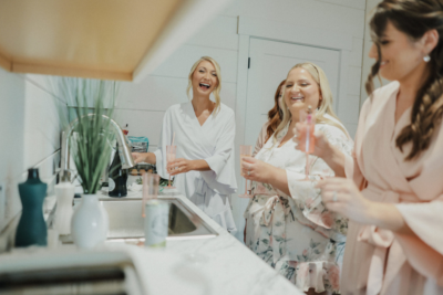 Bride and bridesmaids laughing and sharing champagne toast in the bridal suite kitchenette