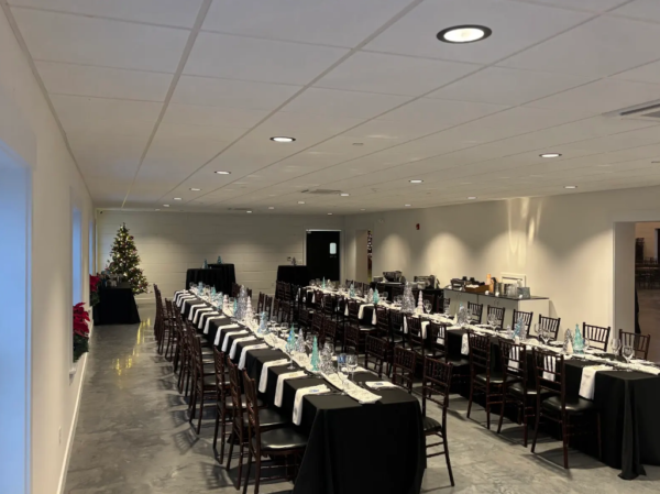 Long banquet dining tables with black linens, winter centerpieces, and holiday tree in the Side Room