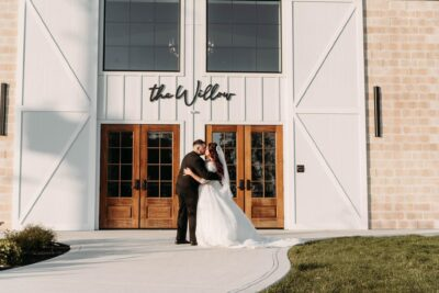 Bride and groom kissing in front of the grand white barn doors and The Willow sign