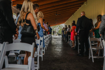 Guests seated under covered timber patio watching bride process down the aisle