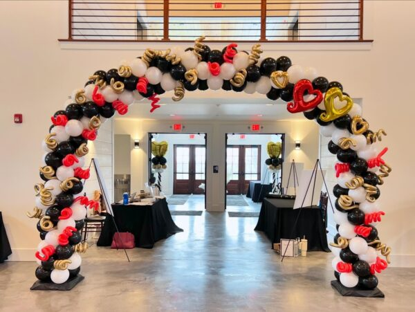 Grand balloon arch in black, red, and gold framing double doors for corporate event celebration