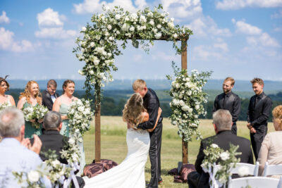 Newlyweds kissing under floral arch with panoramic Laurel Highlands hillside backdrop