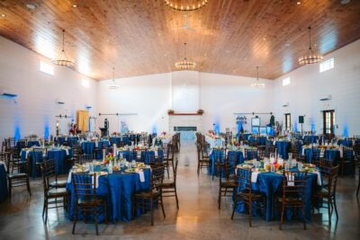 Grand reception hall with wood-paneled ceiling, chandeliers, and royal blue round tables