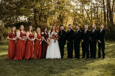 Full wedding party in rust and burgundy dresses with black suits in autumn meadow at The Willow