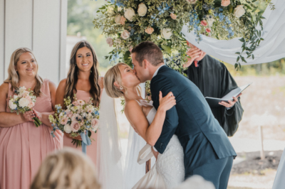 Bride and groom first kiss under floral arch on the covered ceremony patio