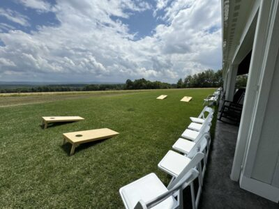 Cornhole lawn games and white ceremony chairs along the covered patio lawn facing Laurel Highlands views