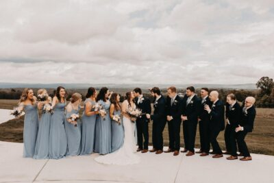 Bride, groom, and wedding party in dusty blue dresses celebrating together on the scenic patio