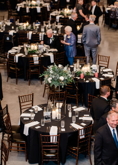 Elevated view of elegant reception dinner tables with black linens, tall floral centerpieces, and glowing candles