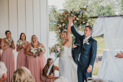 Bride and groom raising hands in celebration at ceremony altar with bridal party