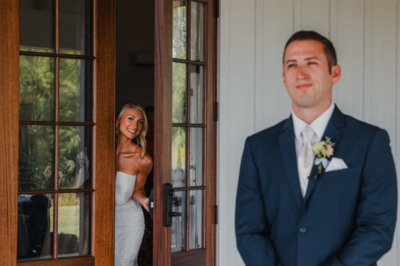 Bride peeking through patio french doors smiling at the groom during wedding first look
