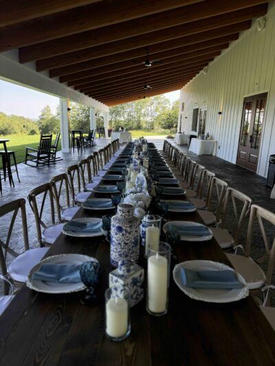 Long banquet table decorated with blue-and-white porcelain vases, pillar candles, and blue napkins on covered patio