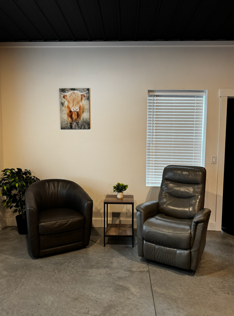 Groom's Den seating nook with leather club chairs, side table, and highland cow artwork