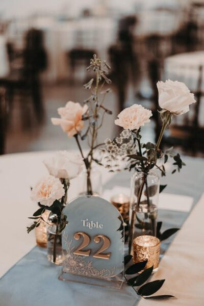 Delicate spring wedding reception table setting with floral bud vases and acrylic Table 22 marker