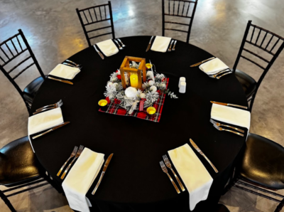 Round banquet table place setting with black linens, wooden lantern centerpiece with candle, and plaid accent