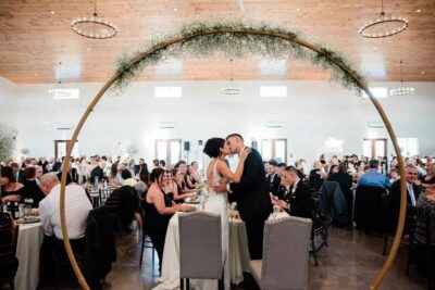Bride and groom sharing a kiss under circular floral greenery arch during wedding reception