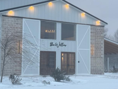 The Willow venue exterior illuminated in a serene winter snowfall with warm sconce lighting
