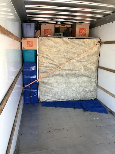 Moving truck interior with strapped mattress, padded furniture, and stacked storage bins