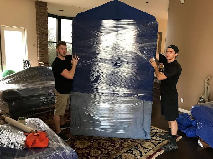 Movers with a completely shrink-wrapped and padded large piece of furniture