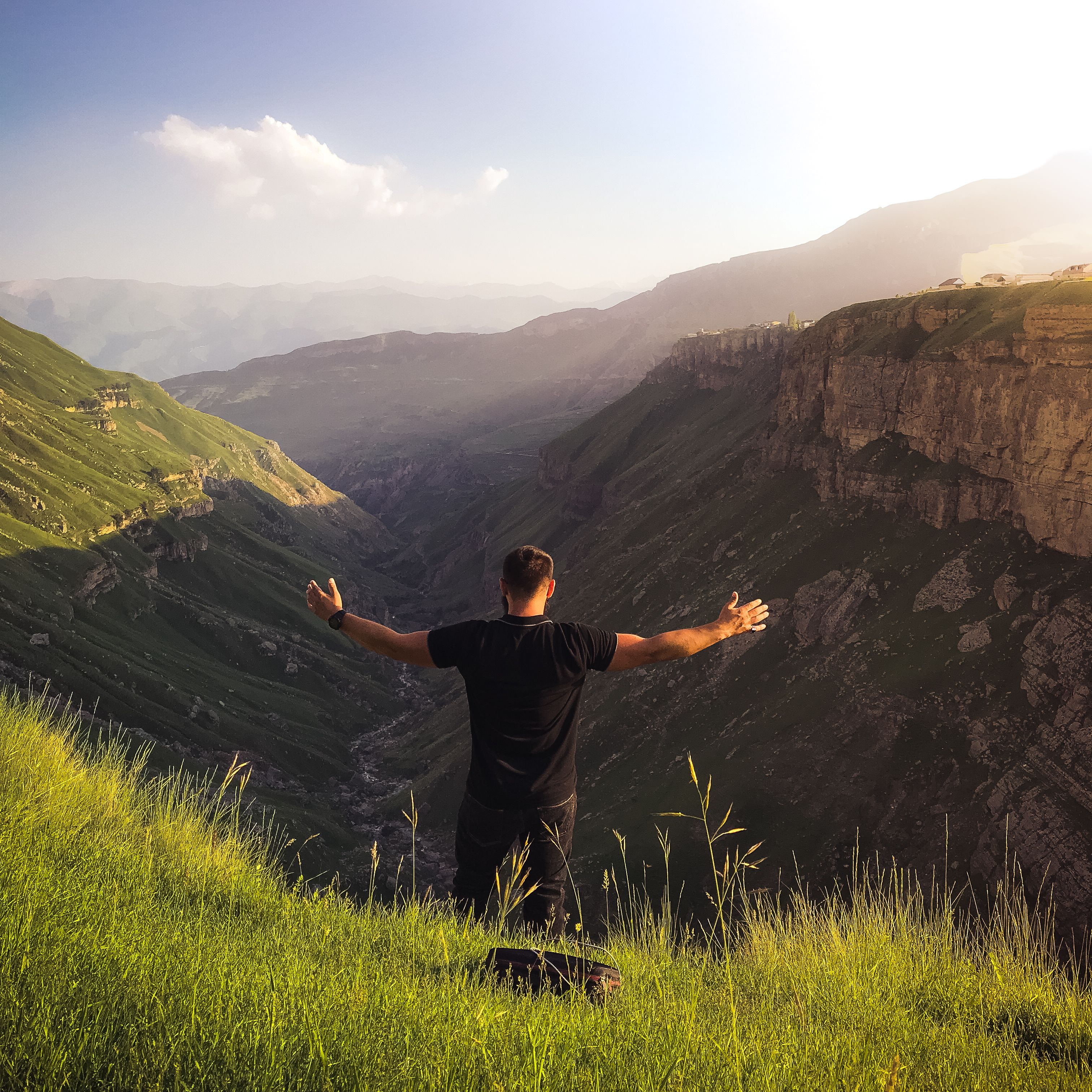 Man standing with arms outstretched overlooking an expansive sunlit mountain canyon