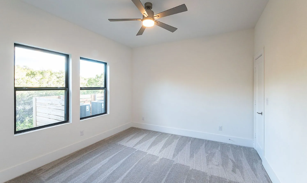 Third bedroom with modern ceiling fan and serene dual-window landscape view