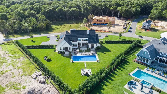 Aerial view of a shingle style home with a rectangular pool, bluestone terrace and hedged lawn