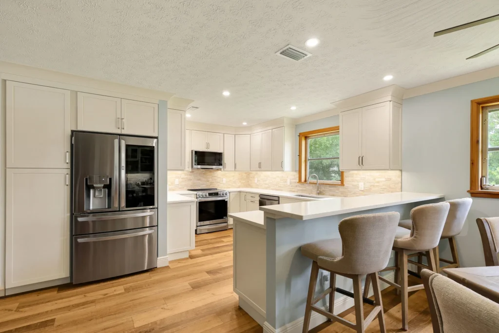 U-shaped white kitchen remodel with a quartz peninsula and hardwood floors by Stuart Kitchen Bath and Flooring
