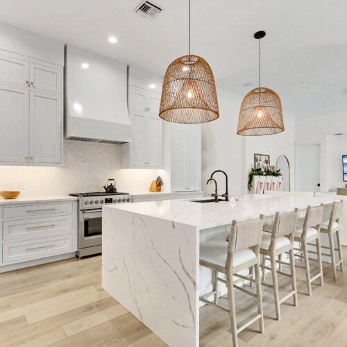 White kitchen remodel with a waterfall island and rattan pendant lights by Stuart Kitchen Bath and Flooring