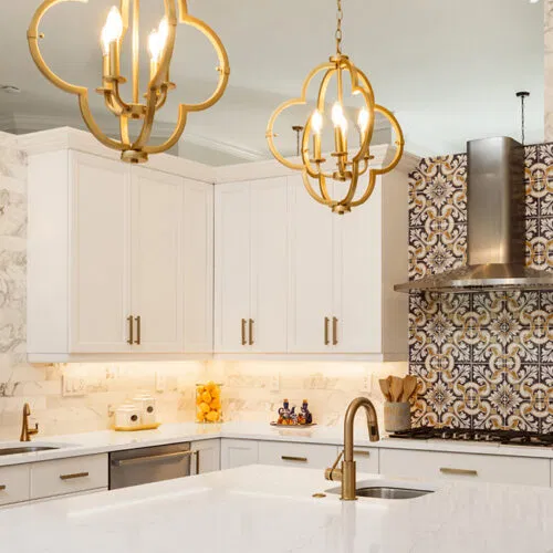 White kitchen remodel with gold pendant lights and a patterned tile backsplash by Stuart Kitchen Bath and Flooring