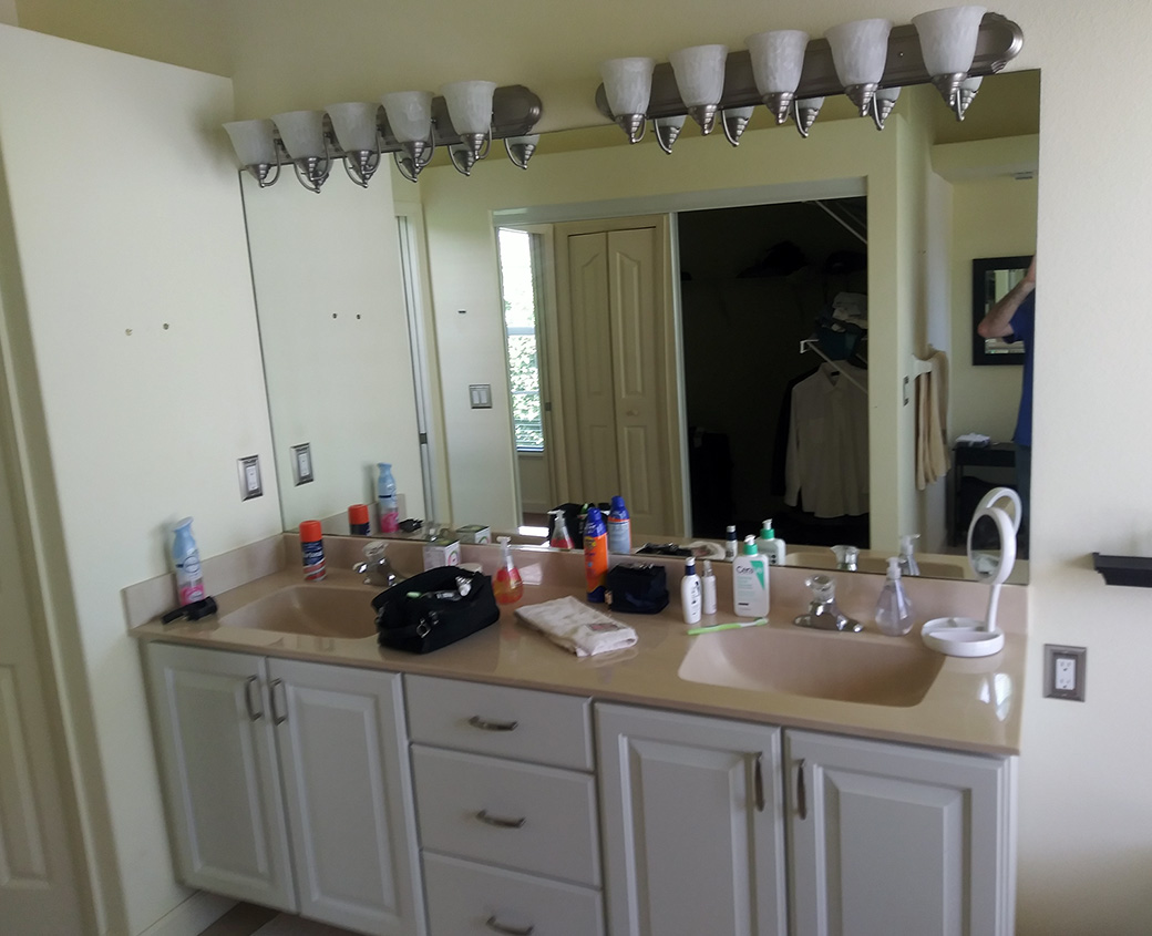 Primary bathroom before renovation, with dated cabinetry, a cultured marble vanity top and an oversized mirror
