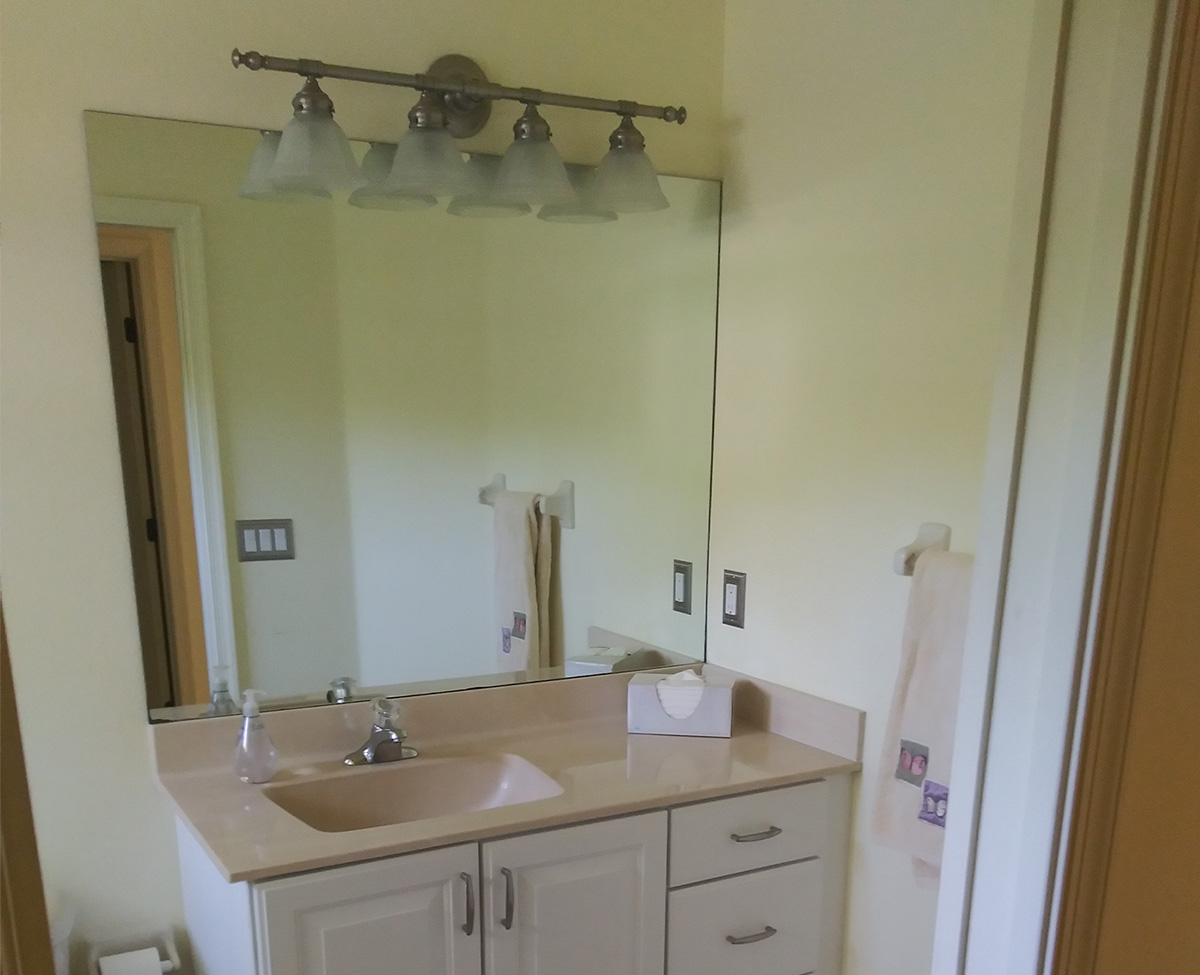 Secondary bathroom before renovation, with a cultured marble vanity top, dated cabinetry and a frameless mirror