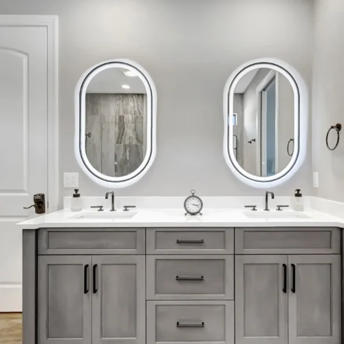 Grey double vanity with oval lit mirrors and matte black hardware by Stuart Kitchen Bath and Flooring