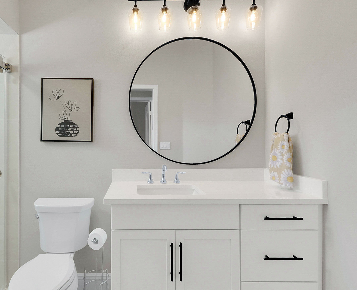 The same secondary bathroom after renovation, with a quartz countertop, shaker cabinetry, black hardware and a round framed mirror