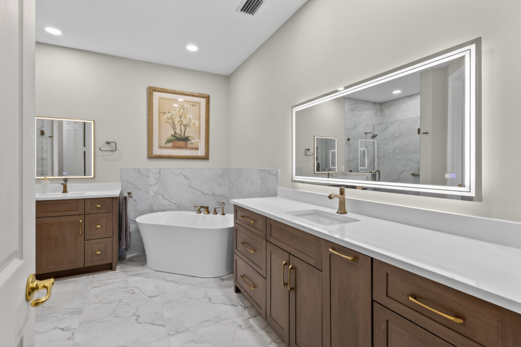 Bathroom remodel with wood vanities, gold fixtures and a freestanding tub by Stuart Kitchen Bath and Flooring