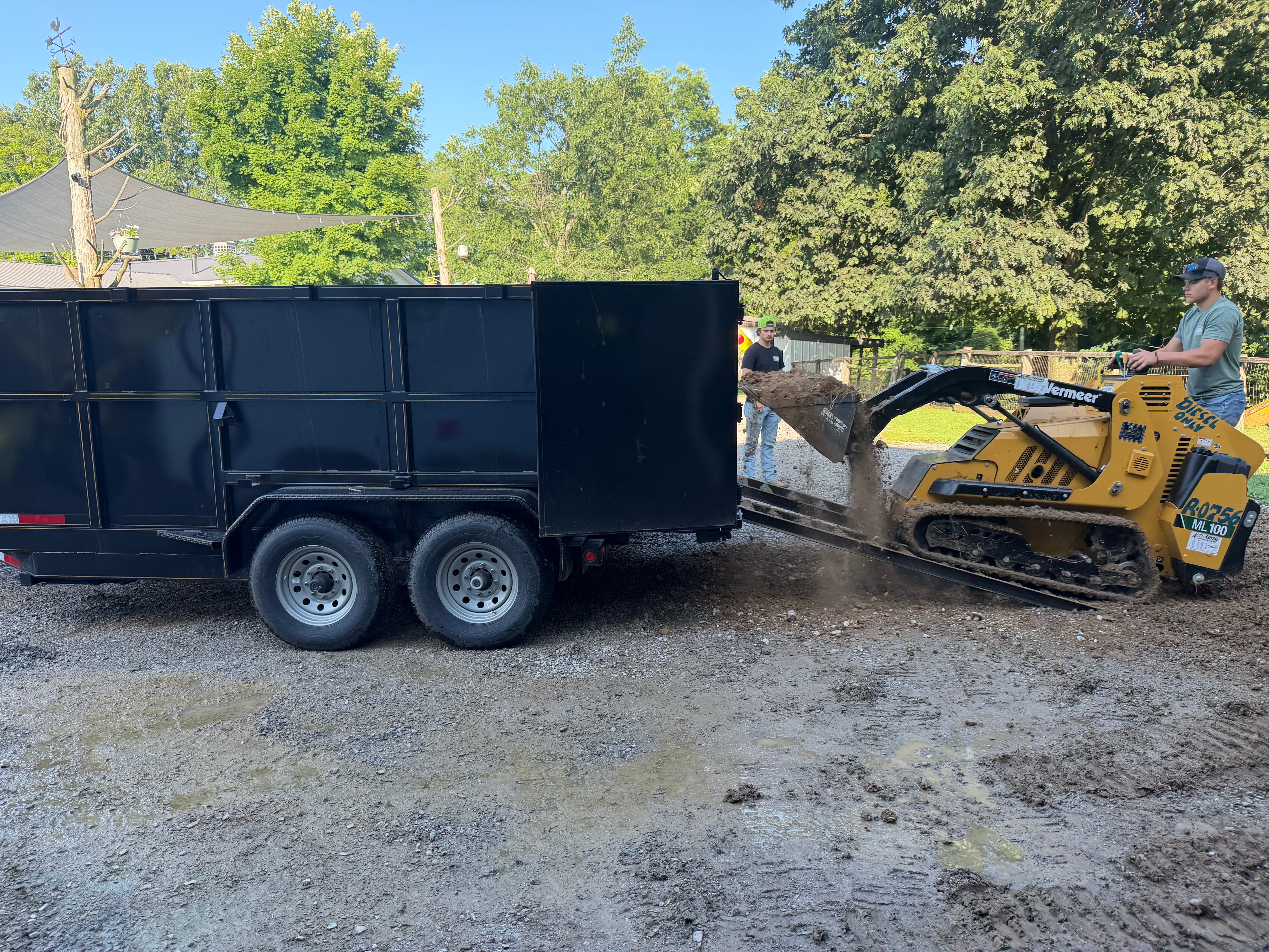 Compact track loader moving and loading dirt into dump trailer on site