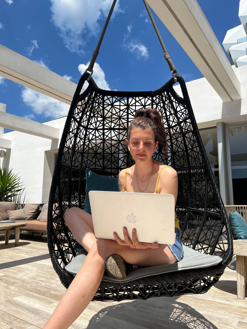 Sara serena all'aperto sulla poltrona sospesa con il MacBook, che gestisce le sue giornate in autonomia