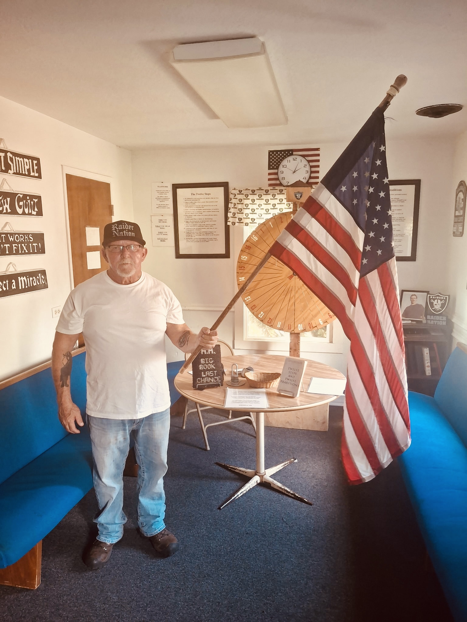 Jeff Galena, Founder of Last Chance AA Group, standing in the meeting room holding the American flag