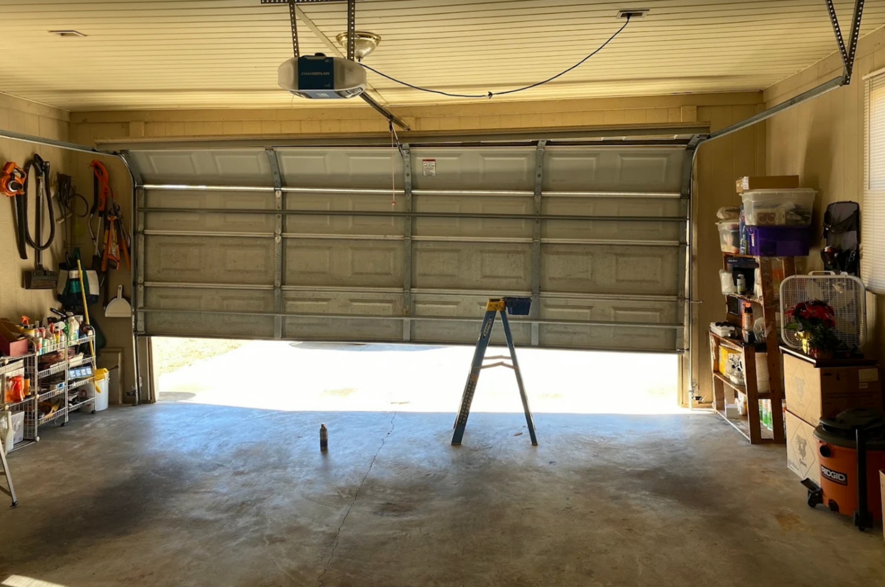 Interior view of a residential garage showing an automatic garage door opener, tracks, and partially raised white sectional door
