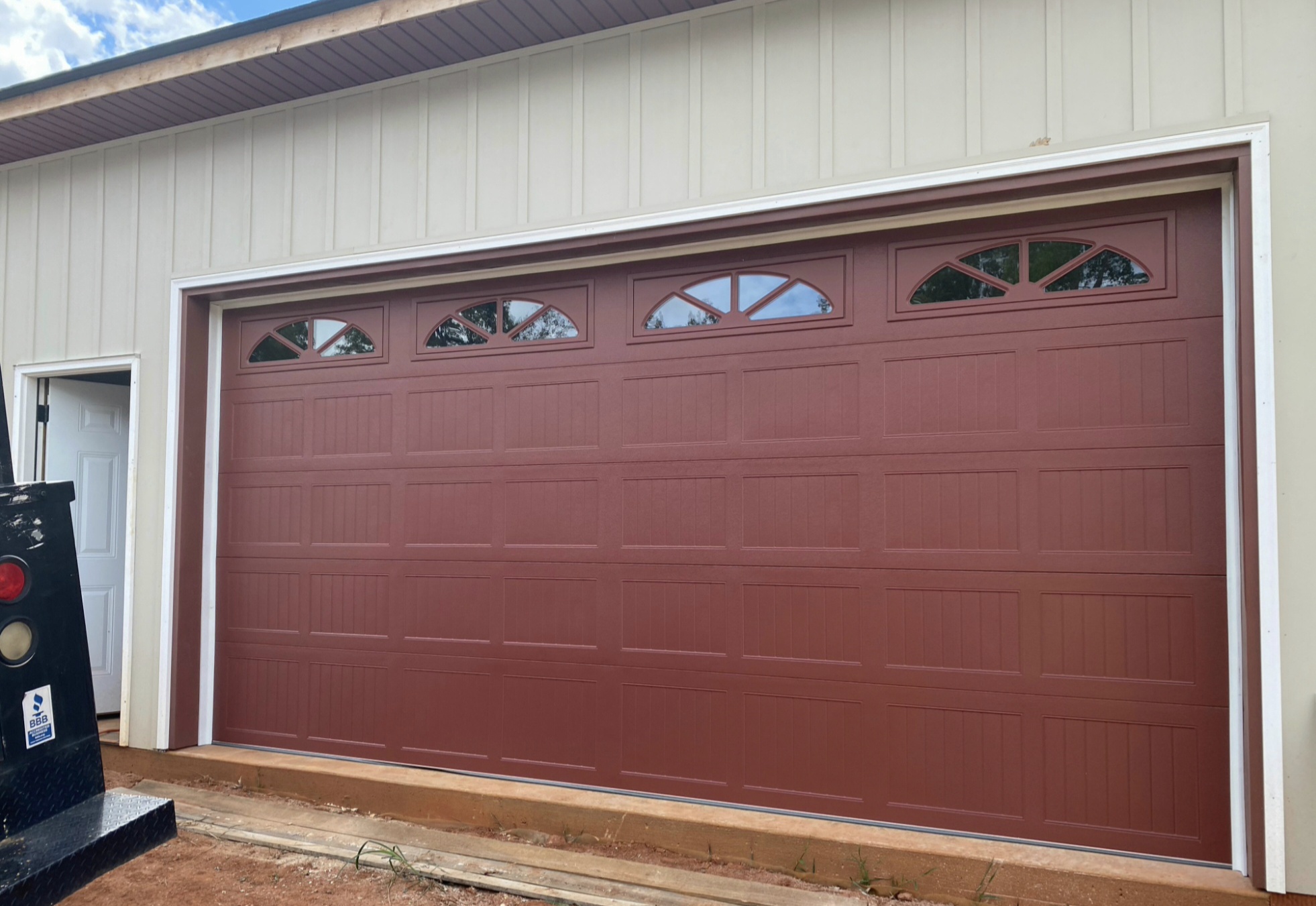 Custom red carriage-house garage door with arched top-panel windows installed on a workshop garage by All Access Garage Doors