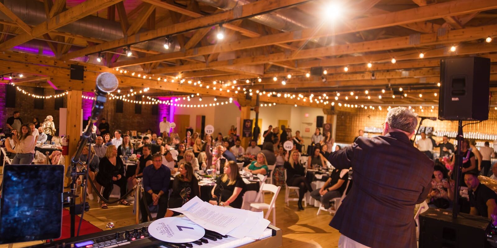 Cincinnati Animal CARE UNLEASHED charity gala fundraiser stage with auctioneer and guests seated at tables in the Rhinegeist event space
