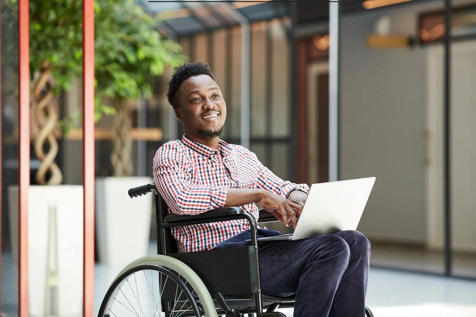 Adult in wheelchair smiling using laptop in bright supportive home environment