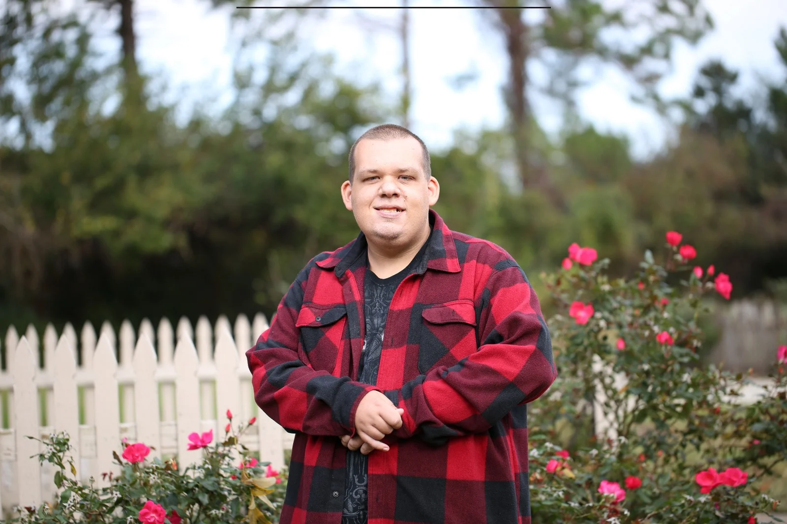 Smiling young adult in red plaid shirt standing outside in a peaceful garden setting